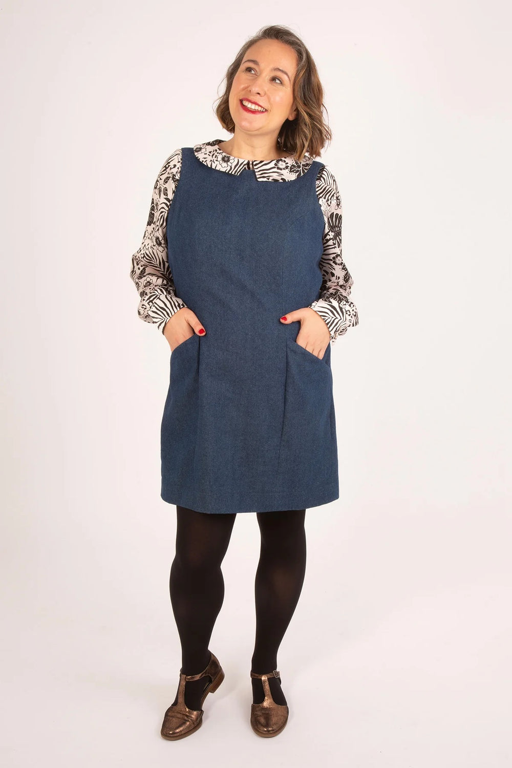 Woman wearing the Clementine Pinafore sewing pattern from Sew Over It on The Fold Line. A sleeveless dress pattern made in denim, corduroy, canvas, or twill fabric, featuring princess seams at the front and back, pockets, and mini length.