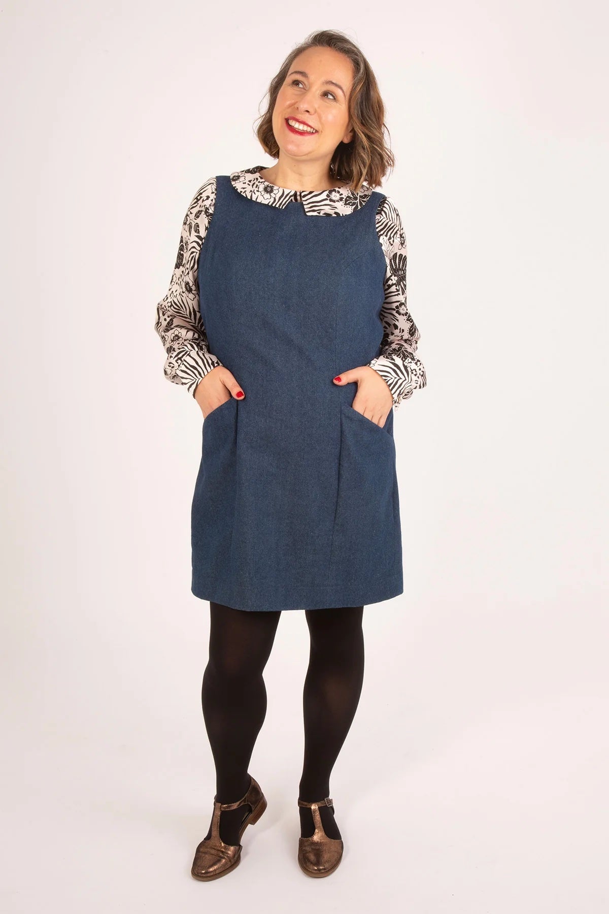 Woman wearing the Clementine Pinafore sewing pattern from Sew Over It on The Fold Line. A sleeveless dress pattern made in denim, corduroy, canvas, or twill fabric, featuring princess seams at the front and back, pockets, and mini length.