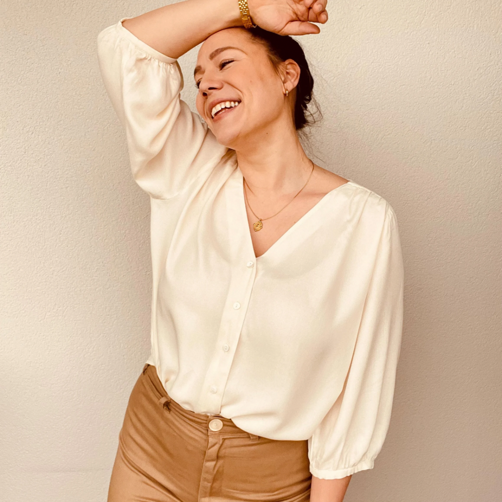 Woman wearing the Cleo Blouse and Top sewing pattern from Sew.lala Patterns on The Fold Line. A top pattern made in linen, poplin, viscose, tencel or silk fabric, featuring a V-neckline, button front, gathered shoulder seams, and 3/4 length sleeves gathered into cuffs.