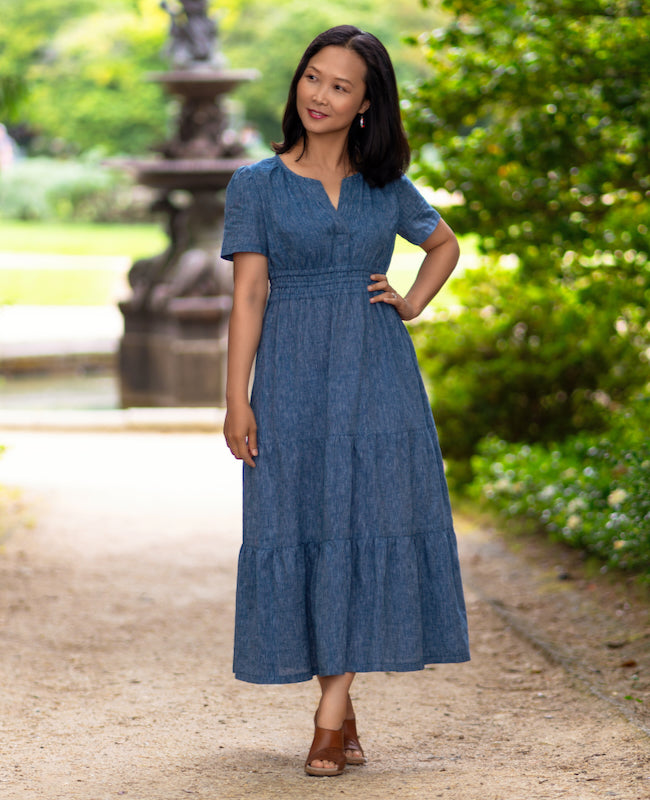 Woman wearing the Comillas Dress sewing pattern from Itch to Stitch on The Fold Line. A dress pattern made in shirting, rayon challis, batiste, chambray, lightweight linen or lightweight broadcloth fabric, featuring a ruffled skirt with three tiers, short gathered sleeves, a gathered front neck with a placket, and a high cinched waist gathered by three rows of elastic.