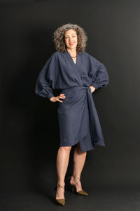 Woman wearing the Copenhagen Wrap Dress sewing pattern from Liesl + Co on The Fold Line. A wrap dress pattern made in cotton poplin, lightweight twill, shirtings, sateen, linen, or double gauze fabric, featuring a blousey top, V-neckline, long voluminous sleeves with cuffs, sarong-style skirt, and knee length.