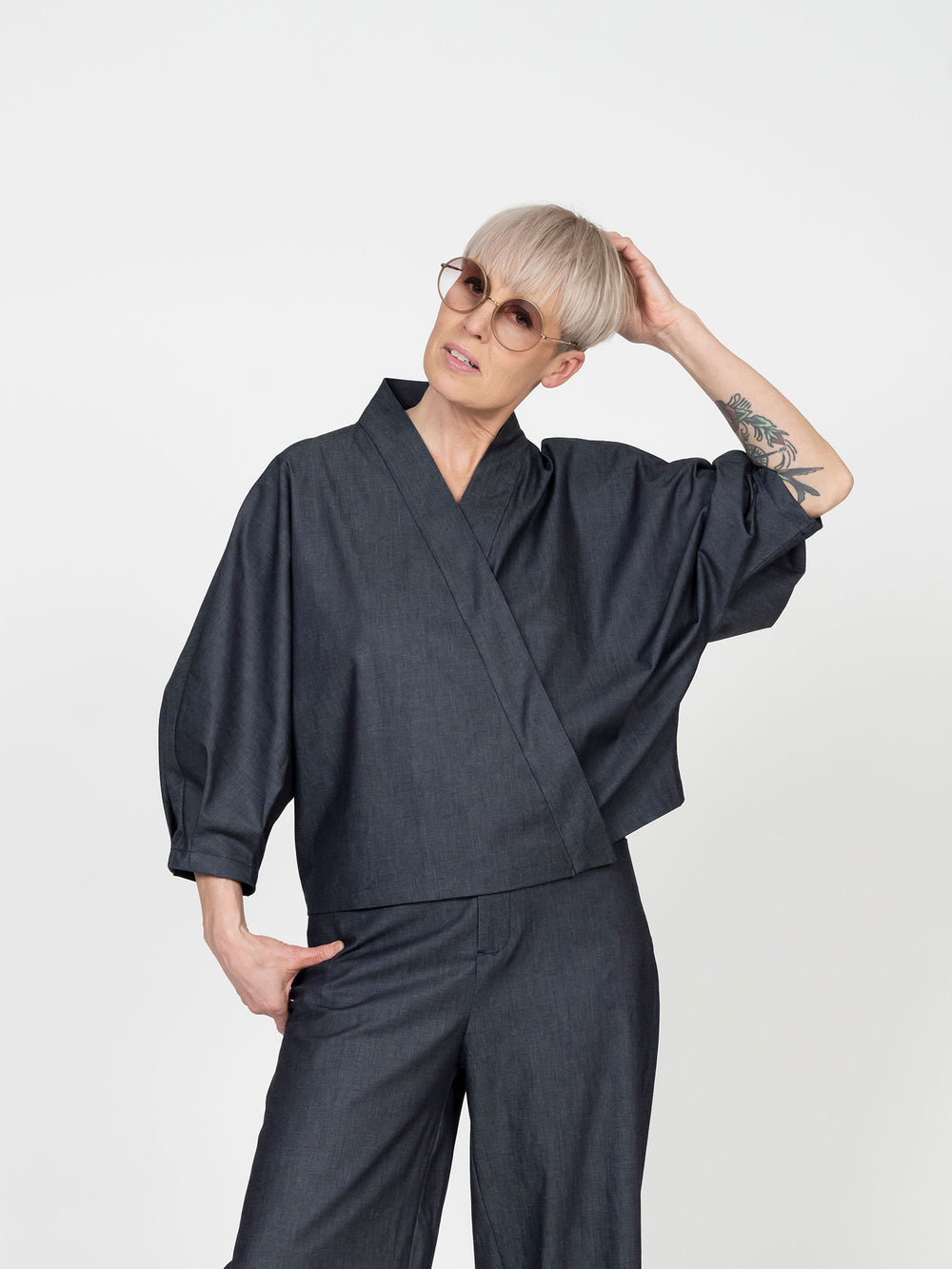 Woman wearing the Cross-Over Shirt sewing pattern from The Assembly Line on The Fold Line. A top pattern made in light to medium weight fabric, featuring a relaxed fit, cross-over front, concealed button closure, three-quarter batwing sleeves, and mid-hip length.