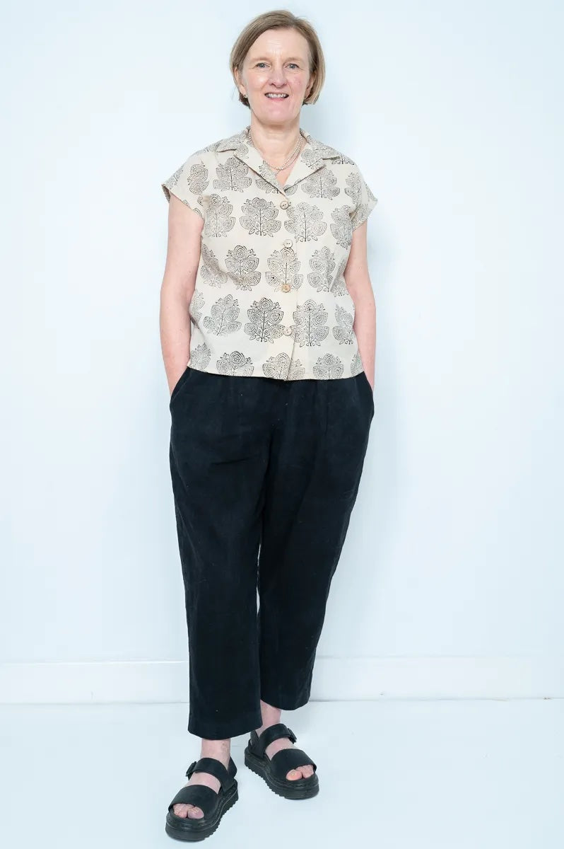 Woman wearing the Debora Blouse sewing pattern from Bobbins and Buttons on The Fold Line. A shirt pattern made in craft weight cotton, chambray, cotton lawn, cotton blend, linen, or linen blend fabric, featuring a V-neck, turn-back collar, bust darts, button front, and grown-on cap sleeves.