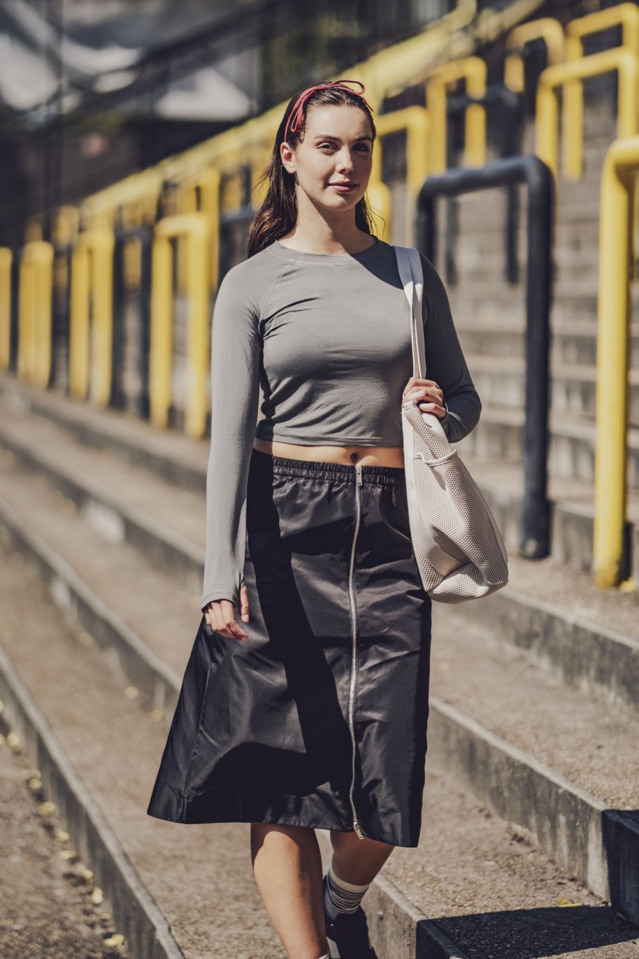 Woman wearing the Dymar Top sewing pattern from Fibre Mood on The Fold Line. A sports top pattern made in stretch jersey, rib knit, power stretch, or sports mesh fabric, featuring a close fit, round neckline, long raglan sleeves with thumbholes, and cropped length.