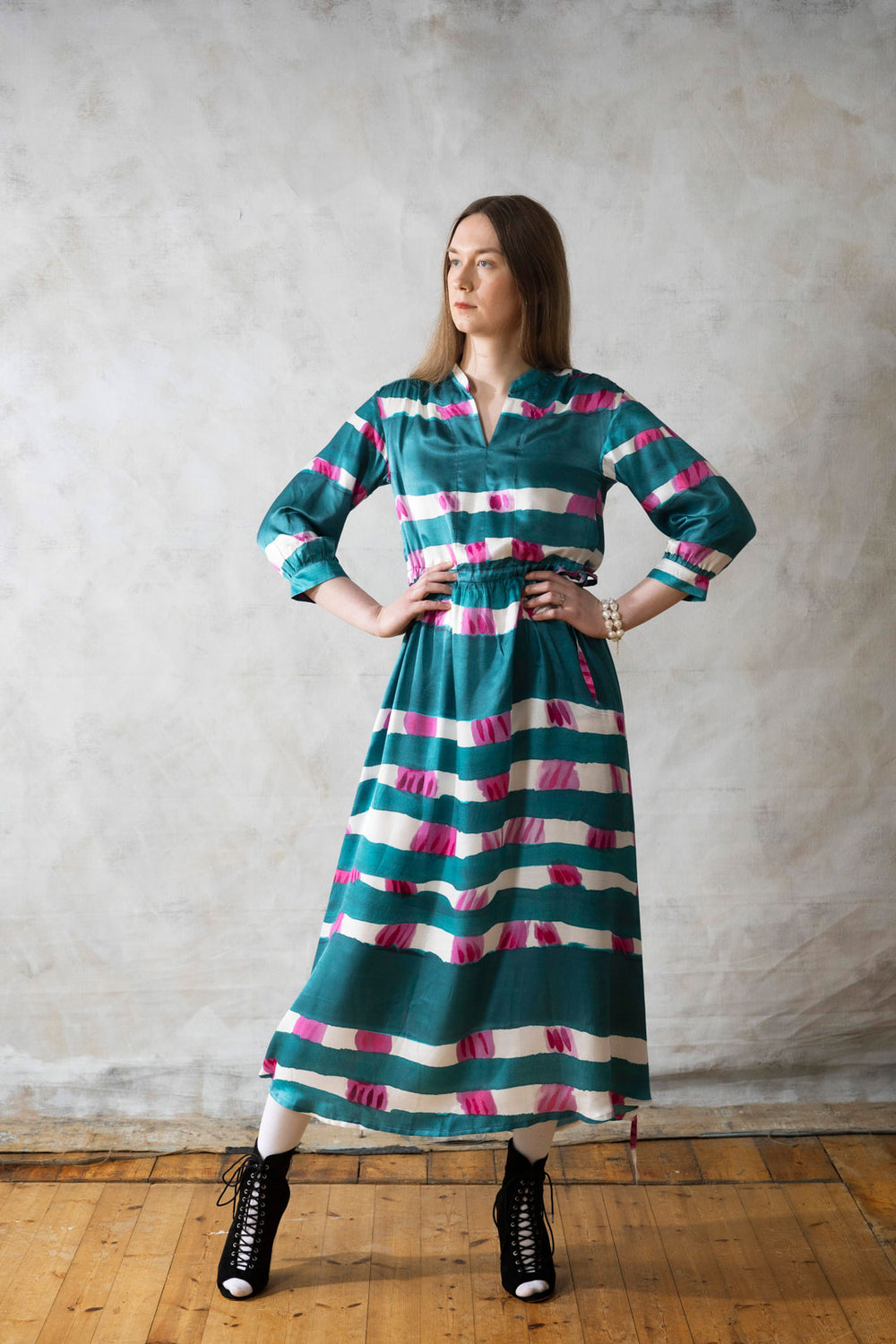 Woman wearing the Dynamo Dress sewing pattern from TAUKO on The Fold Line. A dress pattern made in cotton, linen, satin, silk, or viscose fabric, featuring a band collar, gathered shoulders, drawstring waist with side ties, 3/4 sleeves, side pockets, and midi length.