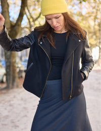 Woman wearing the Electra Jacket sewing pattern from Atelier Scämmit on The Fold Line. A lined biker jacket pattern made in wool, leather, or cashmere fabric, featuring an asymmetric zipper closure, snap-fastened collar, and welt pockets.