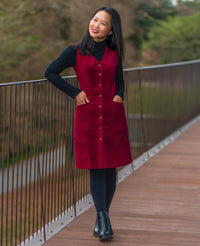 Woman wearing the Elmstead Pinafore sewing pattern from Itch to Stitch on The Fold Line. A sleeveless dress pattern made in corduroy, denim, twill, gabardine, wool or wool blend, sateen, canvas, or stretch suiting fabric, featuring a V-neckline, princess seams, button front, pockets, and knee length.