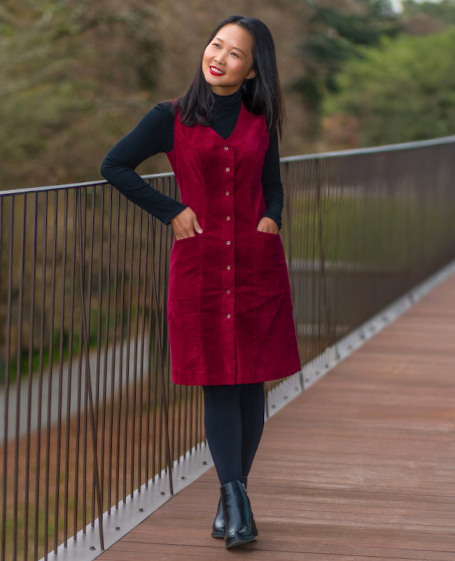 Woman wearing the Elmstead Pinafore sewing pattern from Itch to Stitch on The Fold Line. A sleeveless dress pattern made in corduroy, denim, twill, gabardine, wool or wool blend, sateen, canvas, or stretch suiting fabric, featuring a V-neckline, princess seams, button front, pockets, and knee length.