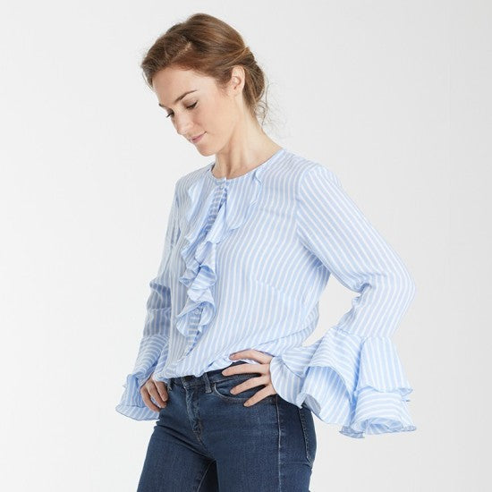 Woman wearing the Élodie Blouse sewing pattern from Coralie Bijasson on The Fold Line. A blouse pattern made in silk, crepe, or cotton voile fabric, featuring a round neckline, front ruffles, button front, and long sleeves with flounces.