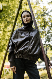 Woman wearing the Elof Jacket sewing pattern from Fibre Mood on The Fold Line. A sleeveless jacket pattern made in leather, denim, wool, or jacquard fabric, featuring a belted collar, front zip, pockets, and elasticated hem.