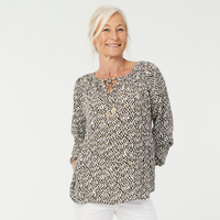 Woman wearing the Elsa Blouse sewing pattern from Coralie Bijasson on The Fold Line. A blouse pattern made in cotton, voile, crepe, or viscose fabric, featuring a gathered neckline with ties and long raglan sleeves with elastic at the wrist.