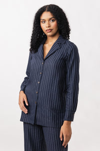 Woman wearing the Elsi Revere Collar Shirt sewing pattern from Named on The Fold Line. A top pattern made in poplin, flannel, or light linen shirting fabric, featuring a deep V-neck, notched lapels, button front, long sleeves with cuffs, and a pleat at the back.