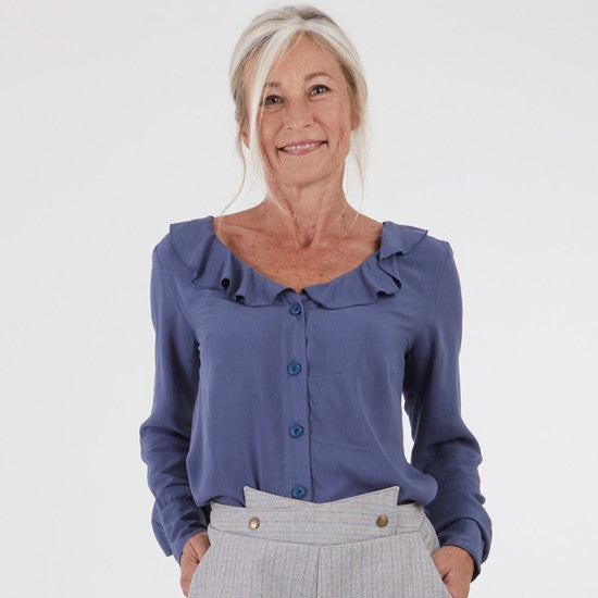 Woman wearing the Emeline Shirt sewing pattern from Coralie Bijasson on The Fold Line. A blouse pattern made in cotton, voile, crepe, or viscose fabric, featuring a ruffled v-neck, button front, and long sleeves with cuffs.