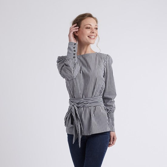 Woman wearing the Emma Blouse sewing pattern from Coralie Bijasson on The Fold Line. A blouse pattern made in batiste, voile, crepe, or satin fabric, featuring a round neckline, long puff sleeves with five-button cuffs, and a self fabric belt.