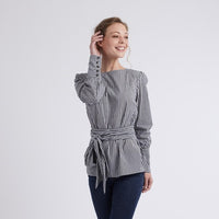 Woman wearing the Emma Blouse sewing pattern from Coralie Bijasson on The Fold Line. A blouse pattern made in batiste, voile, crepe, or satin fabric, featuring a round neckline, long puff sleeves with five-button cuffs, and a self fabric belt.