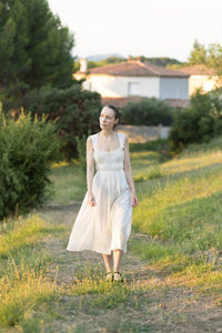 Woman wearing the Emma Dress sewing pattern from Silversaga Patterns on The Fold Line. A sleeveless dress pattern made in cotton voile, cotton lawn, or cotton poplin fabric, featuring  wide shoulder straps, a sweetheart neckline with a ruffle, gathered bodice, elastic waist, and midi length.