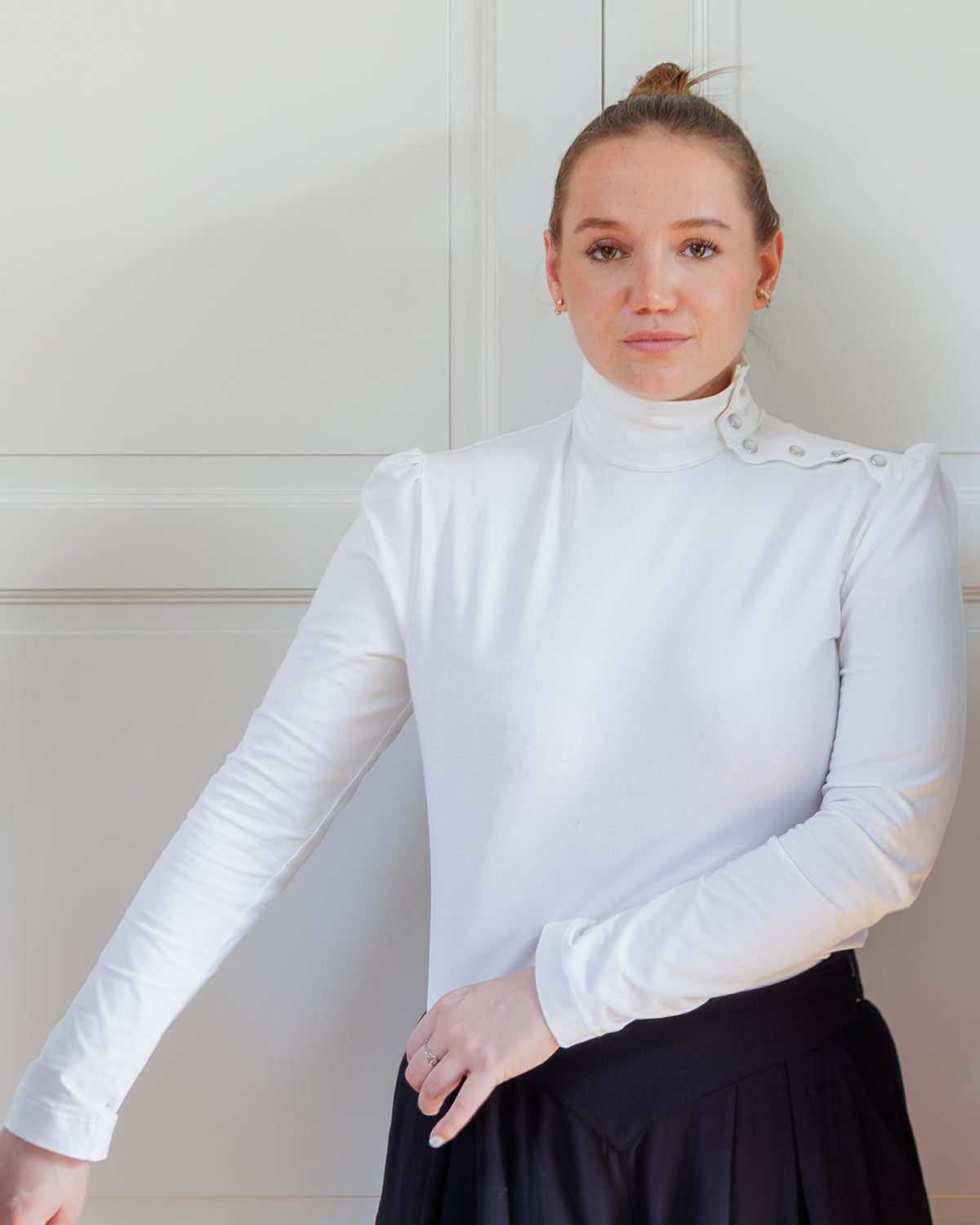 Woman wearing the Erell Top sewing pattern from Coralie Bijasson on The Fold Line. A top pattern made in knit fabric, featuring a mock neck, snap button placket on the left shoulder, and long puff sleeves.