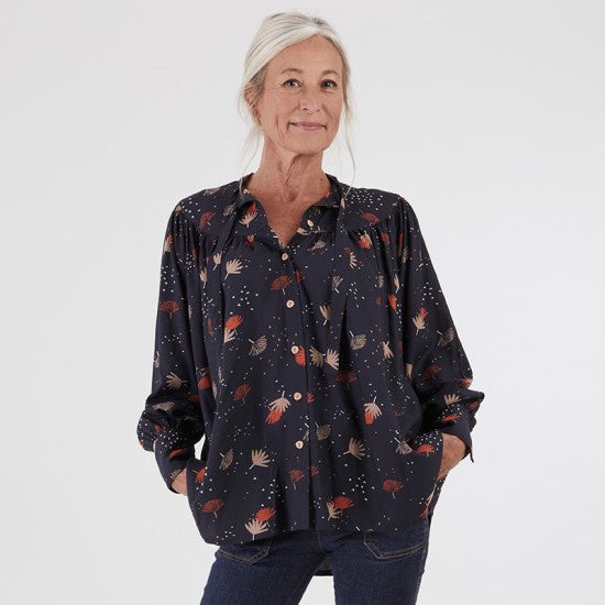 Woman wearing the Erika Blouse sewing pattern from Coralie Bijasson on The Fold Line. A blouse pattern made in viscose crepe, silk satin, or light cotton fabric, featuring a lavallière neckline, rounded front and back yokes, lots of gathering, long sleeves with wide cuffs, and a shirttail hem.