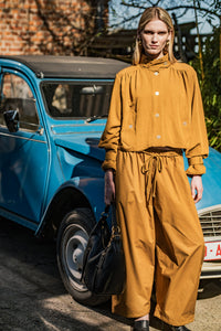 Woman wearing the Evin Jacket sewing pattern from Fibre Mood on The Fold Line. A jacket pattern made in satin, light denim, lyocell, gabardine, or linen fabric, featuring a stand-up collar, front button closure, gathers at the front and back, welt pockets, tabs on the collar and sleeves, and cropped length.