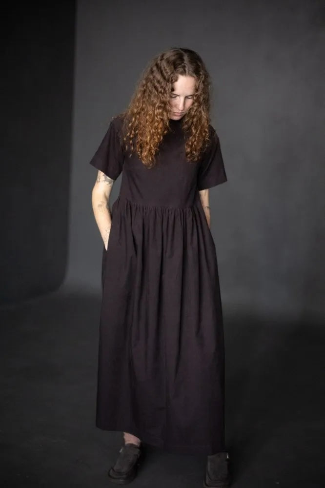 Woman wearing the Fabbrica Dress sewing pattern from Merchant & Mills on The Fold Line. A dress pattern made in linen, linen blend, tencel, cotton chambray, very fine wool, or corduroy fabric, featuring a loose fit, boat neck, short sleeves, long gathered skirt, and in-seam pockets.