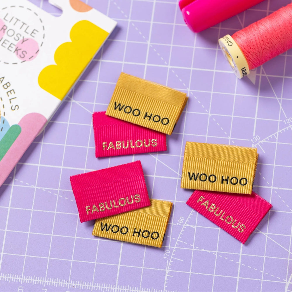 The 'Fabulous / Woo Hoo' woven labels from Little Rosy Cheeks on The Fold Line. The pack includes 6 labels in fuchsia and gold with a 3D ribbed texture, ready to be sewn into your handmade clothes.