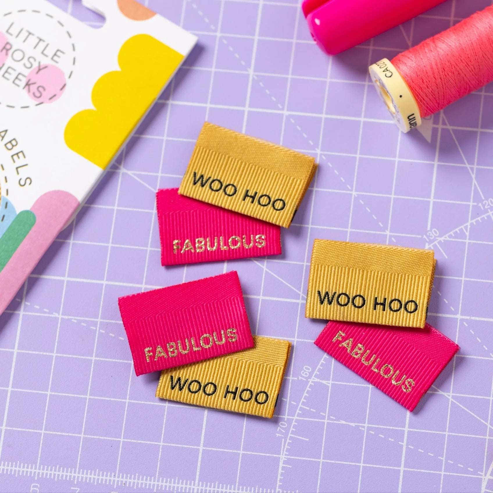 The 'Fabulous / Woo Hoo' woven labels from Little Rosy Cheeks on The Fold Line. The pack includes 6 labels in fuchsia and gold with a 3D ribbed texture, ready to be sewn into your handmade clothes.