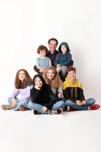 A man, teens, and children wearing the Family Ada Sweatshirt sewing pattern from Schnittchen Patterns on The Fold Line. A sweatshirt pattern made in sweatshirt fabric, featuring a ribbed neckband or hood, long sleeves, and colour blocking options.