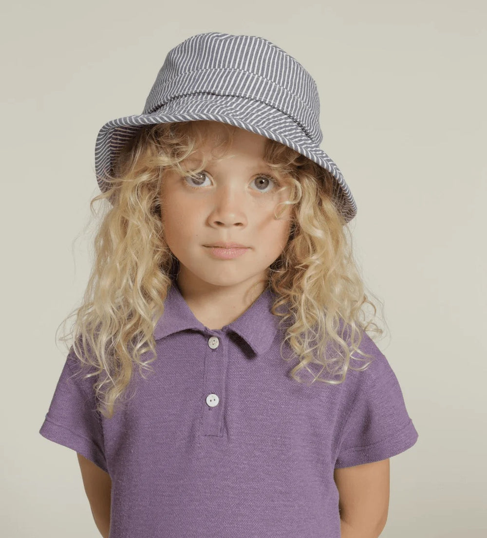 Child wearing the Family Safari and Bucket Hats sewing pattern from Wardrobe by Me on The Fold Line. A hat pattern made in canvas, cotton drill, or denim fabric, featuring a lining, decorative band, and stitch details and binding around the brim.