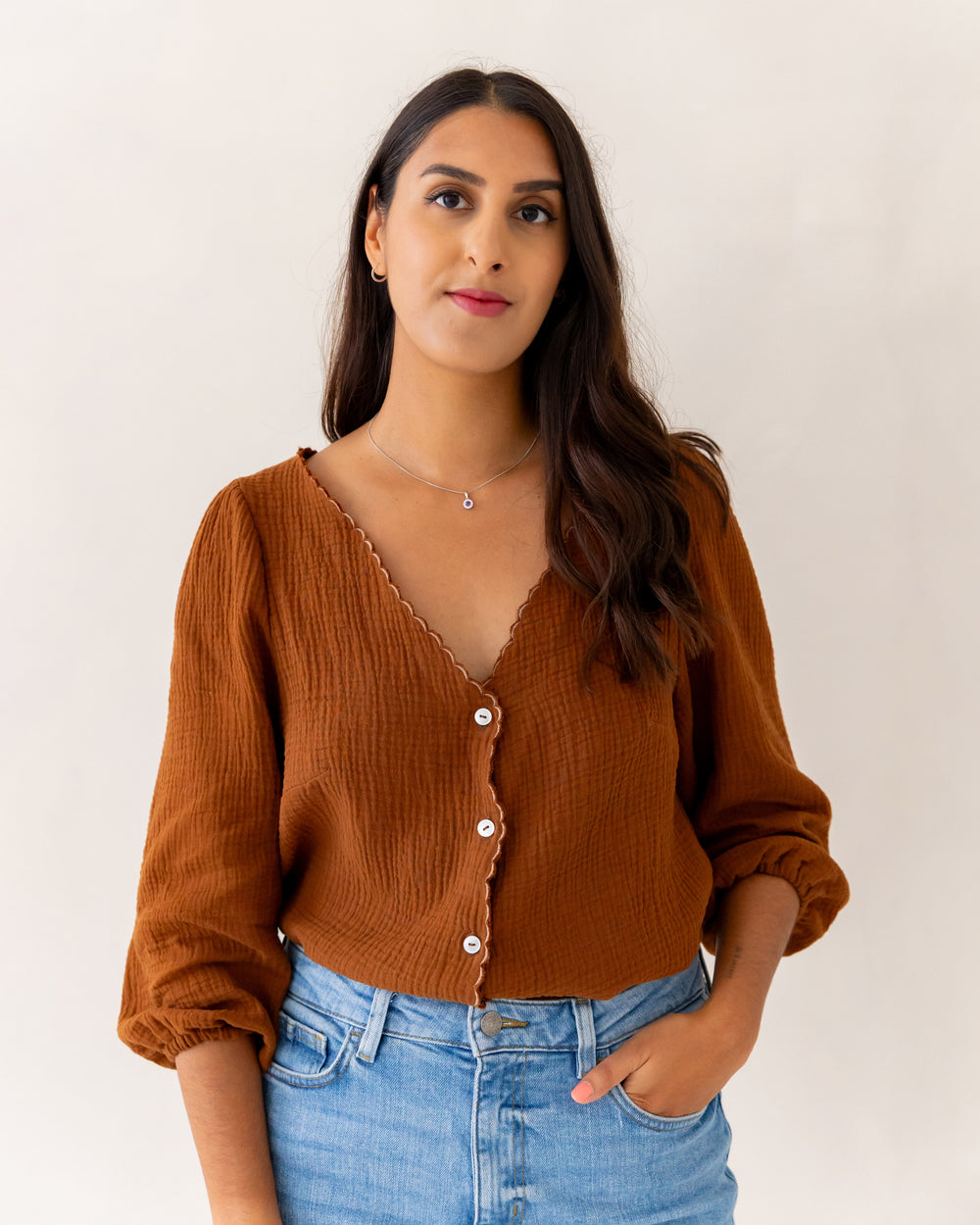 Woman wearing the Faye Blouse sewing pattern from Tammy Handmade on The Fold Line. A top pattern made in cotton, linen, twill, double gauze, or viscose fabric, featuring a V-neck, button front, and 3/4 length puff sleeves.