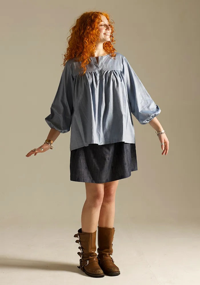 Woman wearing the Felis Blouse sewing pattern from Sew Different on The Fold Line. A top pattern made in cotton, cotton lawn, linen, or viscose fabric, featuring a relaxed fit, placket opening, gathering above the bust, and 3/4 sleeves with elasticated cuffs.