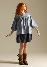 Woman wearing the Felis Blouse sewing pattern from Sew Different on The Fold Line. A top pattern made in cotton, cotton lawn, linen, or viscose fabric, featuring a relaxed fit, placket opening, gathering above the bust, and 3/4 sleeves with elasticated cuffs.