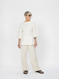 Woman wearing the Fitted Waist T-shirt sewing pattern from The Assembly Line on The Fold Line. A top pattern made in jersey fabric, featuring a boat neckline, dropped shoulders, wide elbow-length sleeves, and a shaped waist with topstitched pleats at the front and back.