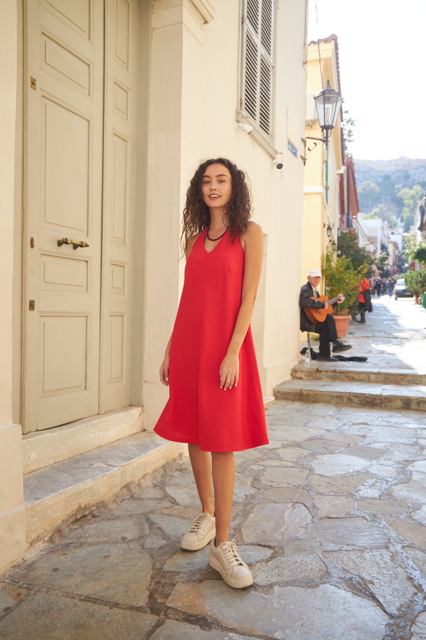 Woman wearing the Flora Dress sewing pattern from The Patterns Room on The Fold Line. A sleeveless dress pattern made in linen, viscose, satin, or crepe fabric, featuring an A-line silhouette, halter neck, V-neckline, bust darts, and knee length.