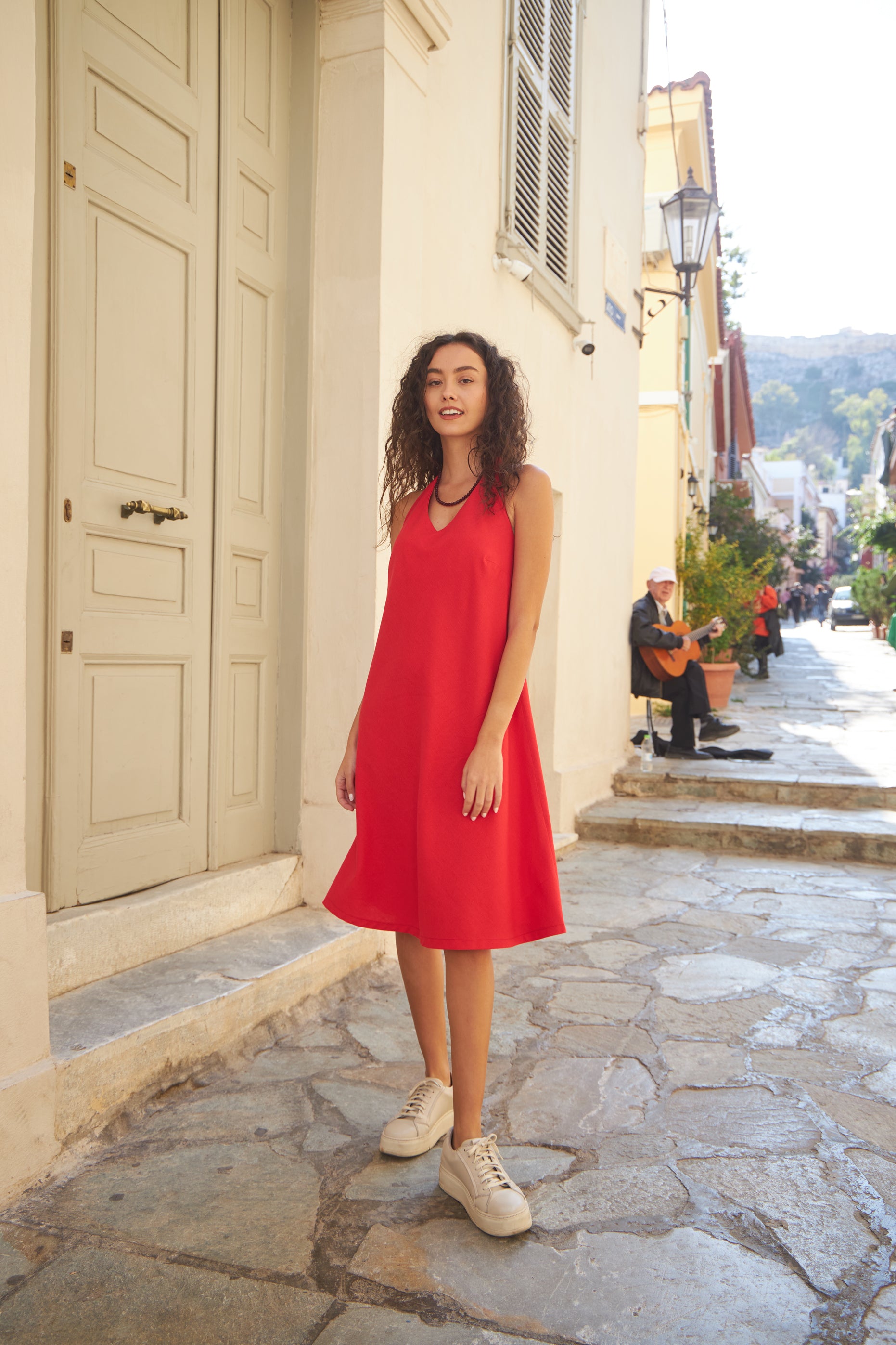 Woman wearing the Flora Dress sewing pattern from The Patterns Room on The Fold Line. A sleeveless dress pattern made in linen, viscose, satin, or crepe fabric, featuring an A-line silhouette, halter neck, V-neckline, bust darts, and knee length.