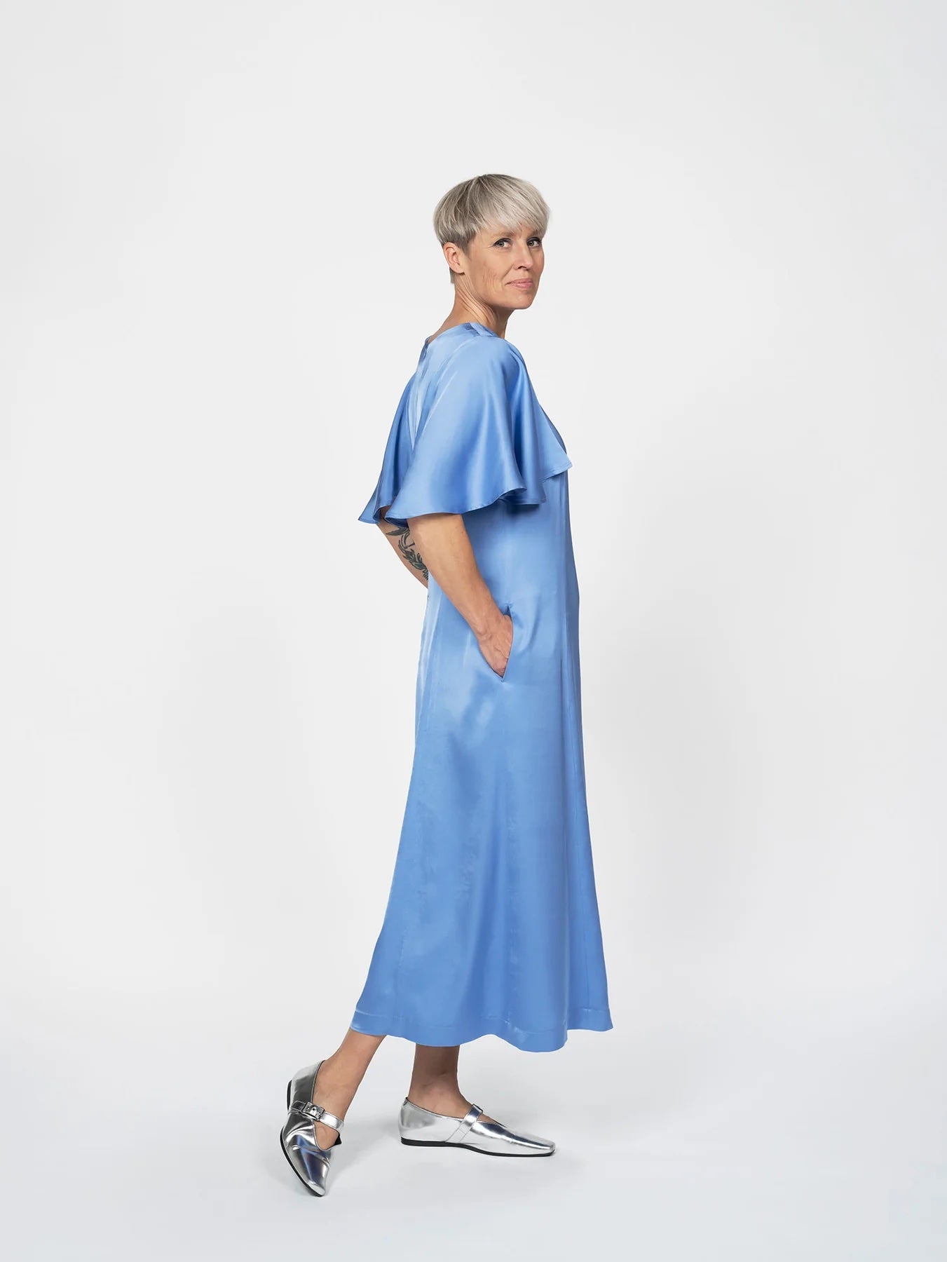 Woman wearing the Flutter Sleeve Dress sewing pattern from The Assembly Line on The Fold Line. A dress pattern made in light to medium weight fabric, featuring a round neckline, flutter sleeves, slightly A-line skirt, side seam pockets, and midi length.