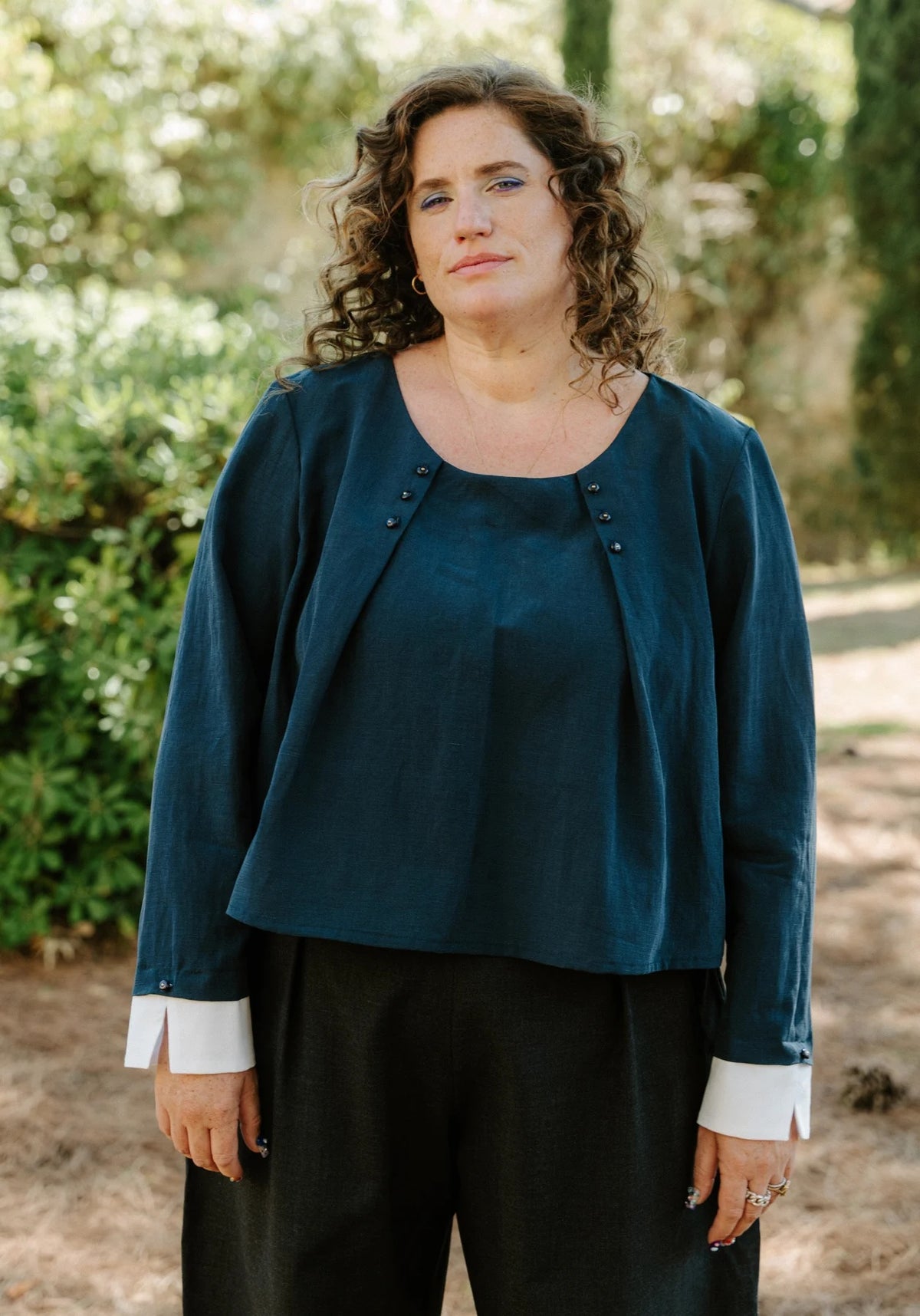 Woman wearing the Folio Blouse sewing pattern from Maison Fauve on The Fold Line. A top pattern made in viscose, soft jacquard, tencel, cotton, crepe, poplin, satin, or twill fabric, featuring a round neckline with pleats and buttons and long sleeves with contrast cuffs.