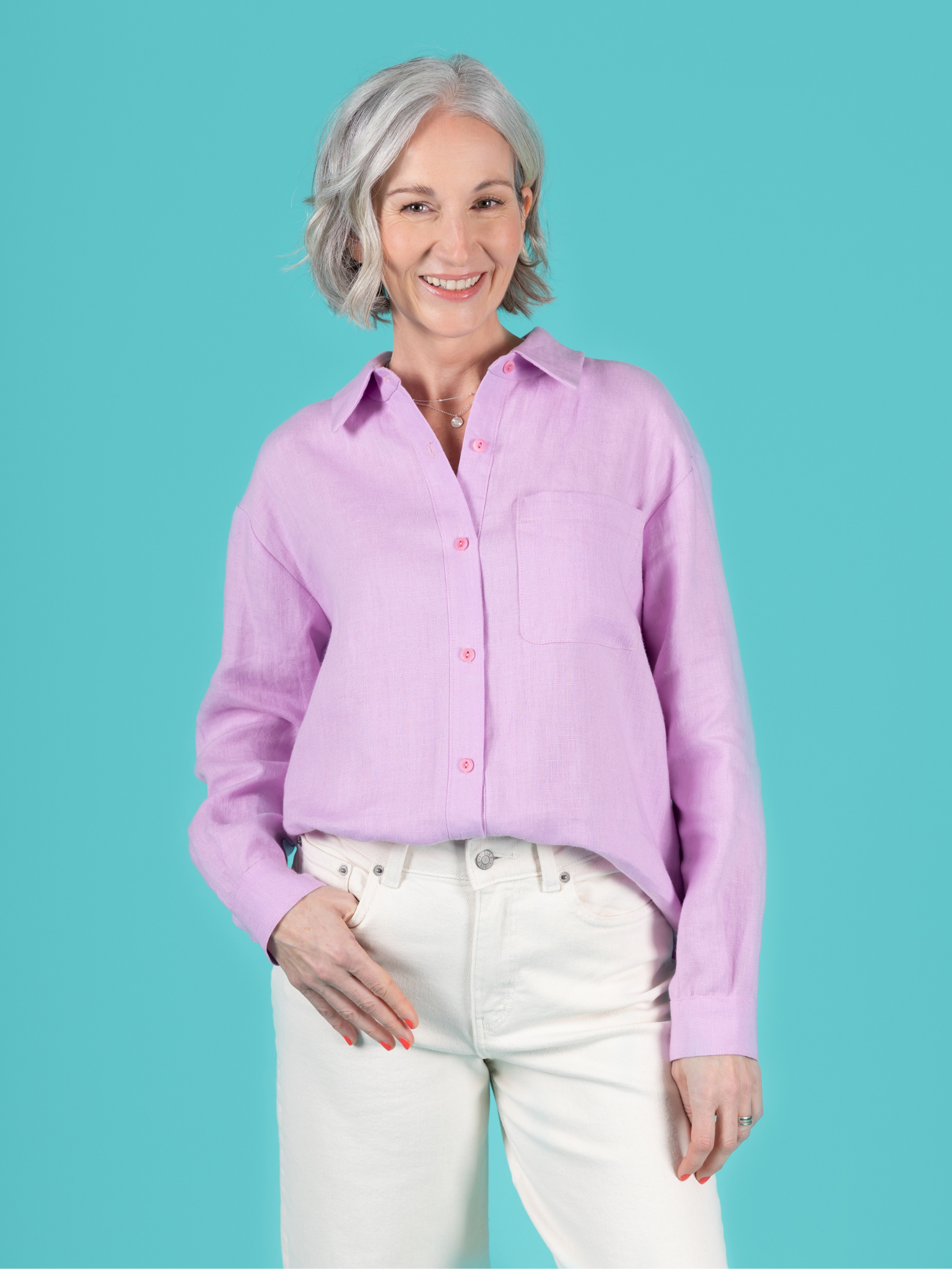 Woman wearing the Frida Shirt sewing pattern from Tilly and the Buttons on The Fold Line. A shirt pattern made in cotton lawn, poplin, dobby, shirting, chambray, flannel, fine needlecord, washed linen, or viscose (rayon) fabric, featuring a relaxed fit, dropped shoulders, button front, two-piece collar and stand, long sleeves pleated into cuffs with plackets, and a curved patch pocket.