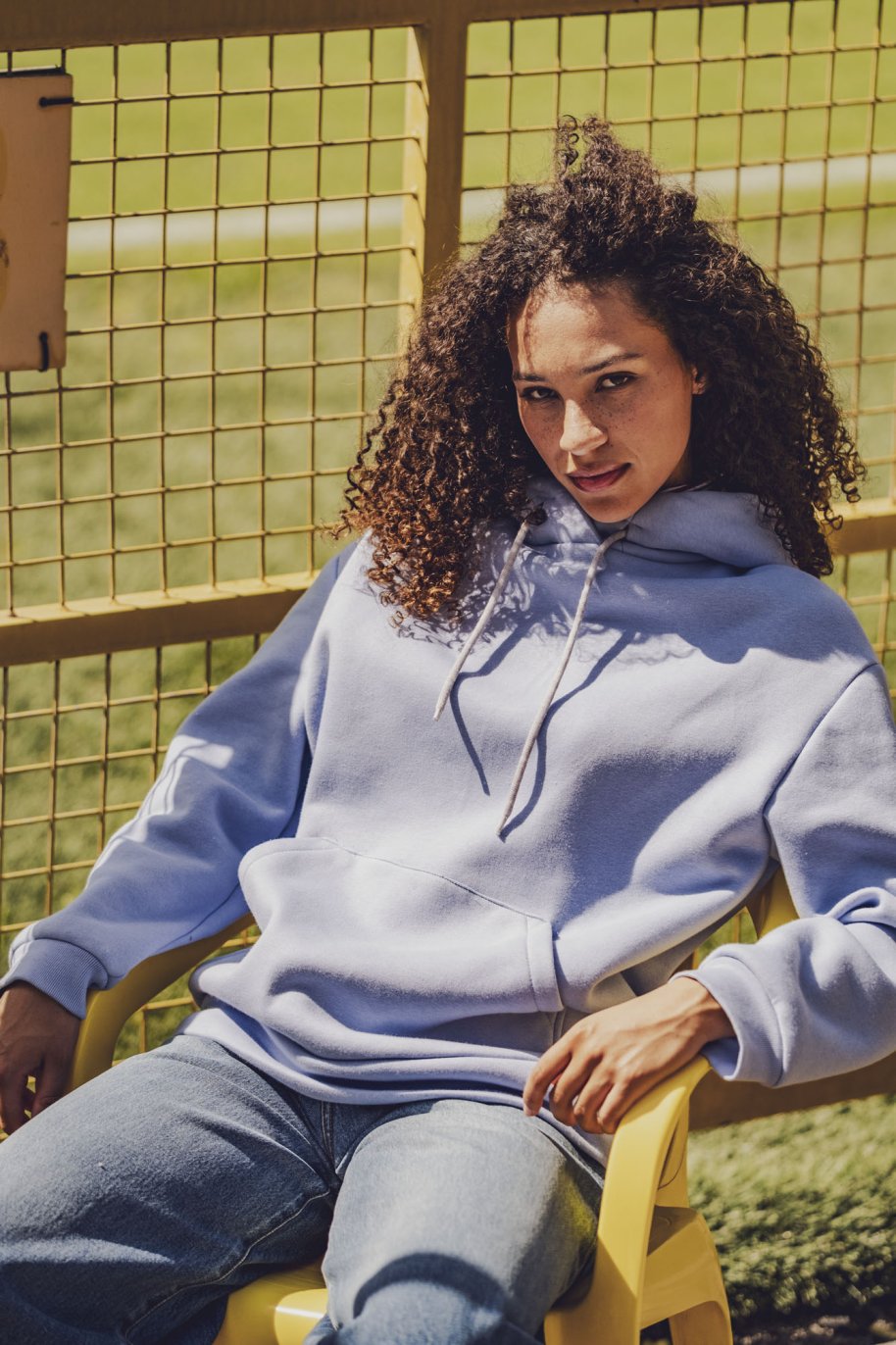 Woman wearing the Fritzi Hoodie sewing pattern from Fibre Mood on The Fold Line. A hoodie pattern made in sweater fabric, French terry, punto di Roma, scuba, lightweight neoprene, or teddy fabric, featuring a relaxed fit, long sleeves, kangaroo pocket, and hood with a drawstring.