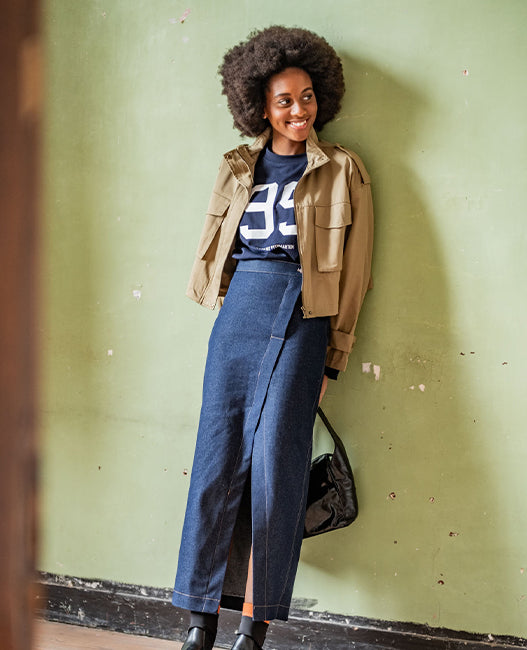Woman wearing the Fulki Skirt sewing pattern from Fibre Mood on The Fold Line. A skirt pattern made in cotton twill, denim, leather, velvet, or wool fabric, featuring an asymmetric design, button fastening, back darts, patch pockets, decorative topstitching, and maxi length.