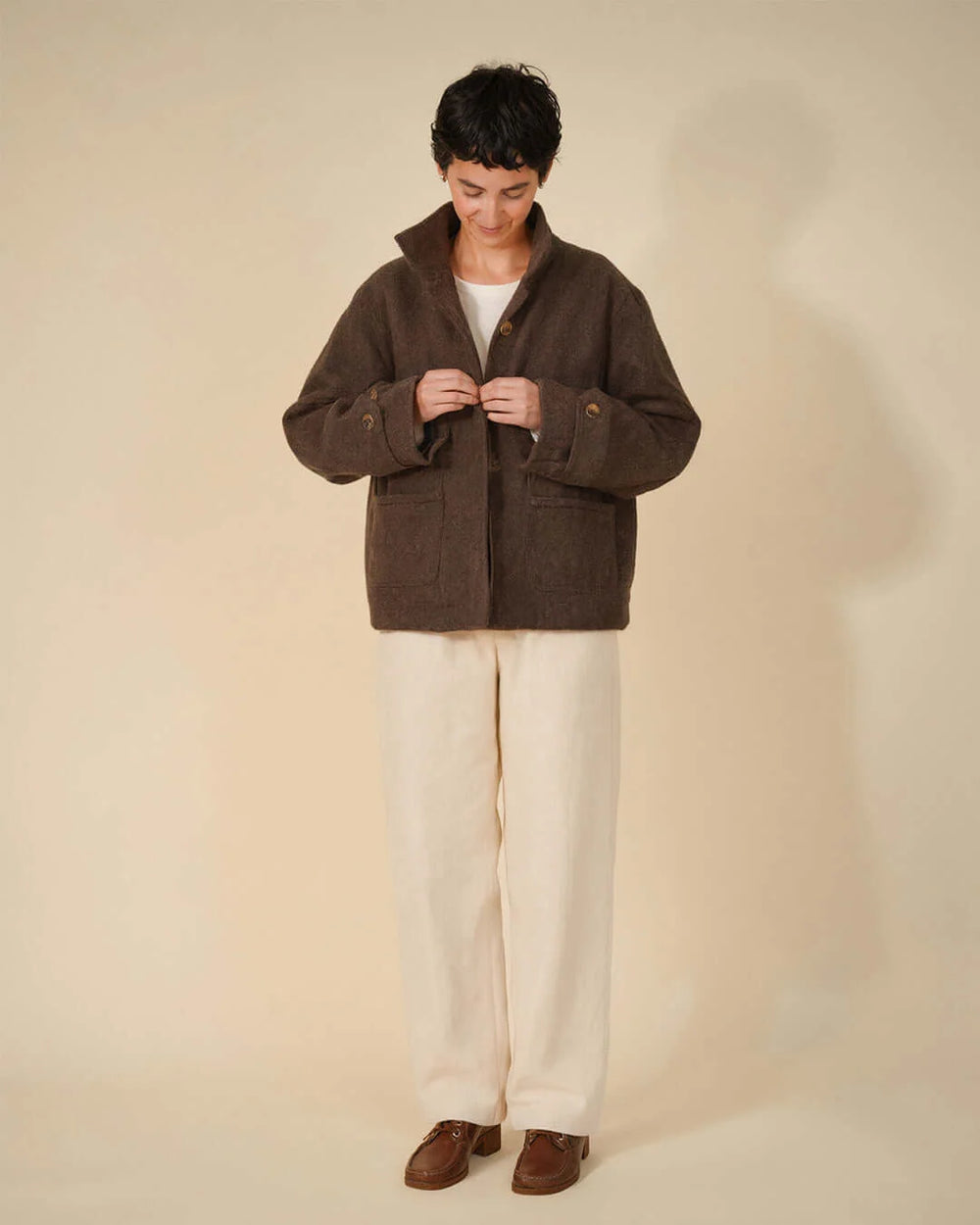 Woman wearing the Funnel Neck Jacket sewing pattern from Wardrobe by Me on The Fold Line. A fully lined jacket pattern made in waxed cotton, wool, cotton twill, canvas, corduroy, denim, or nylon fabric, featuring a relaxed fit, high collar, concealed button closure, patch pockets, and two-piece sleeves with adjustable button tabs.
