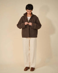 Woman wearing the Funnel Neck Jacket sewing pattern from Wardrobe by Me on The Fold Line. A fully lined jacket pattern made in waxed cotton, wool, cotton twill, canvas, corduroy, denim, or nylon fabric, featuring a relaxed fit, high collar, concealed button closure, patch pockets, and two-piece sleeves with adjustable button tabs.
