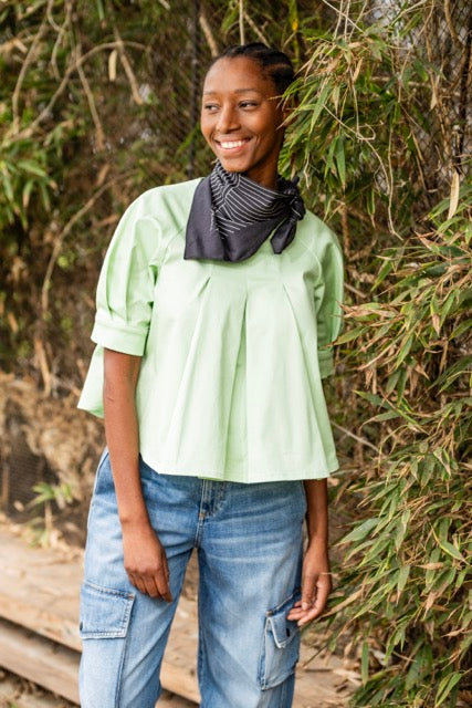 Woman wearing the Georgie Top sewing pattern from Fibre Mood on The Fold Line. A blouse pattern made in lyocell, poplin, or woven jacquard fabric, featuring an A-line silhouette, front and back pleats, and short raglan balloon sleeves with cuffs.