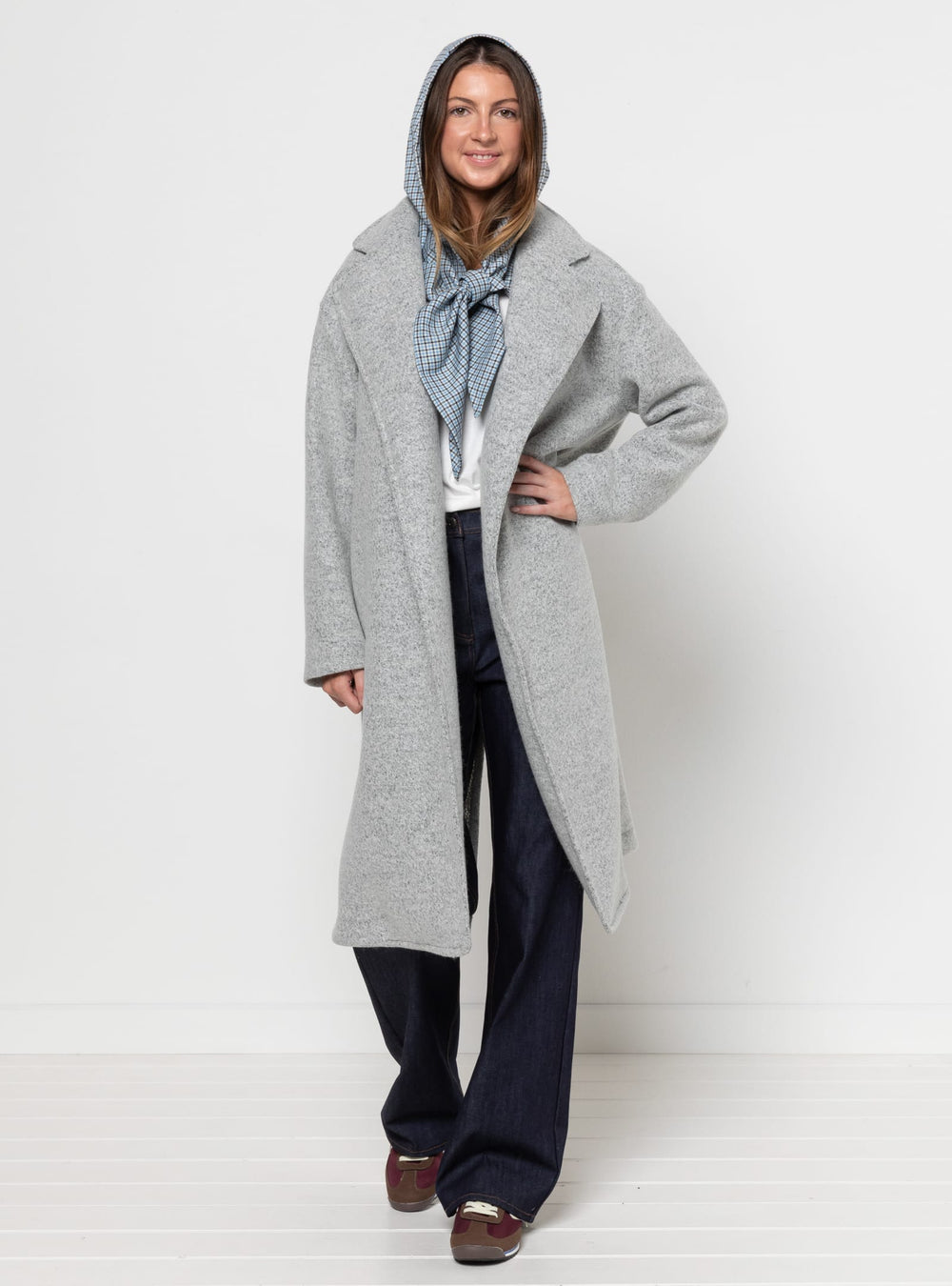 Woman wearing the Gracie Coat and Headscarf sewing pattern from Style Arc on The Fold Line. An unlined coat pattern made in gabardine, denim, heavy linen, cotton drill, corduroy, boiled wool, tweed wool, or ponte knit fabric, featuring a boxy fit, revere collar, wrap front, dropped shoulders, and two-piece sleeves.