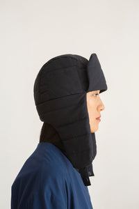 Woman wearing the Greet Hat sewing pattern from TAUKO on The Fold Line. A trapper hat pattern made in medium weight woven fabric, featuring quilting and ear flaps.