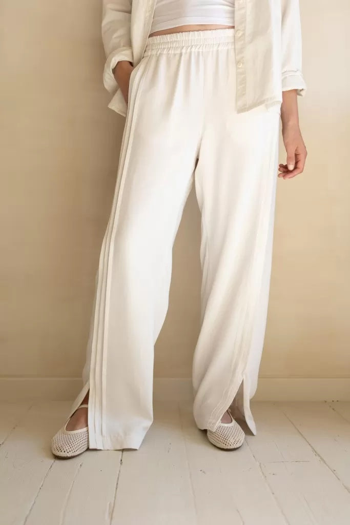 Woman wearing the Hadid Couture Track Pants sewing pattern from Ready to Sew on The Fold Line. A pants pattern made in tencel or linen/tencel fabric, featuring a relaxed fit, elasticated waistband, pintuck stripes, pockets, and zips at the ankles.
