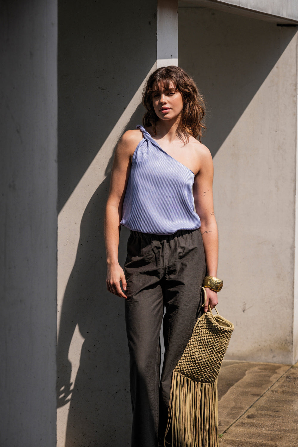 Woman wearing the Hallie Top sewing pattern from Fibre Mood on The Fold Line. A one-shoulder top pattern made in poplin, (silk) satin, double gauze, linen, chambray, or lyocell fabric, featuring a draped twist effect at the shoulder.