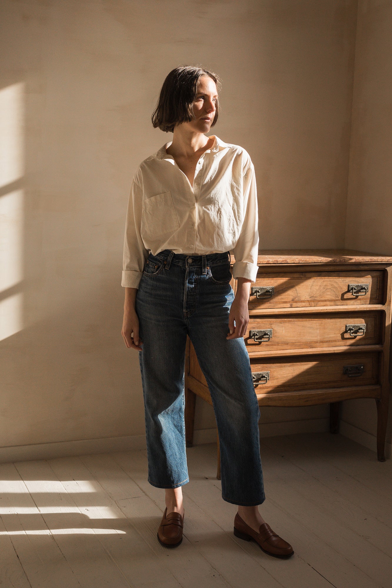 Woman wearing the Hans Shirt sewing pattern from Ready to Sew on The Fold Line. A shirt pattern made in cotton poplin, oxford, chambray, linen, or lightweight denim fabric, featuring a classic cut with an oversized fit, collar, button front, chest pocket, long sleeves with plackets, and side vents.