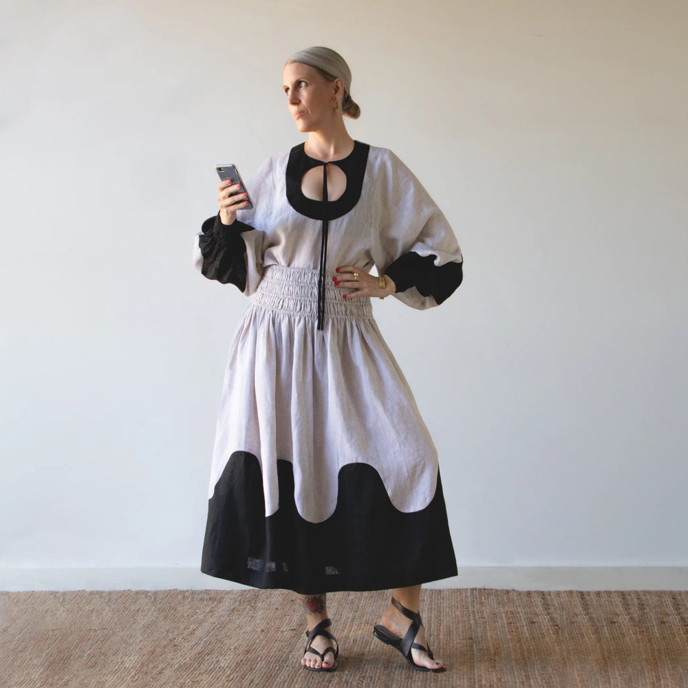 Woman wearing the Harmonic Set sewing pattern from Pattern Fantastique on The Fold Line. A top and skirt pattern made in linen or cotton fabric, featuring a top with a circular keyhole neckline and balloon sleeves with faux-shirred cuffs, and skirt with a faux-shirred waistband, pockets, and midi length.