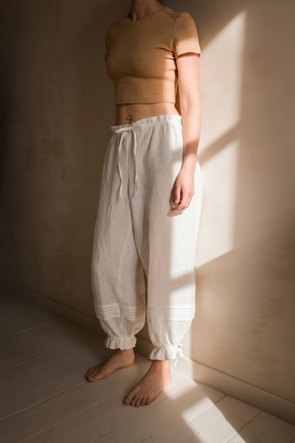 Woman wearing the Harper Pants sewing pattern from Ready to Sew on The Fold Line. A vintage-inspired pants pattern made in cotton, linen, tencel, or viscose fabric, featuring a billowy silhouette, paper bag waist with a drawstring, and pintucks and adjustable ties at the ankles.