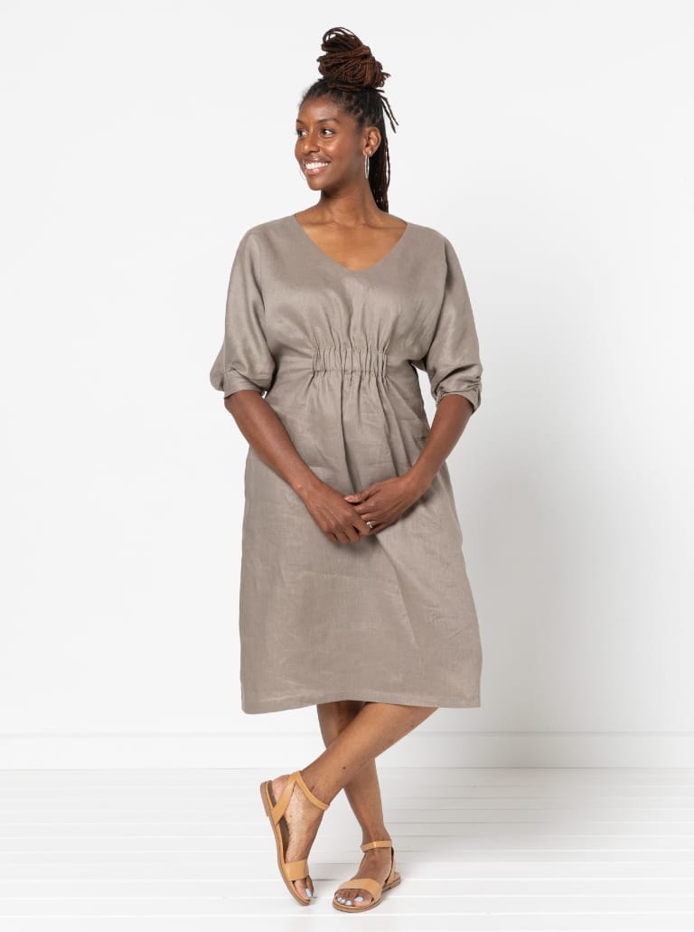 Woman wearing the Harry Woven Dress sewing pattern from Style Arc on The Fold Line. A dress pattern made in linen, rayon, silk, or crepe fabric, featuring a slight A-line shape, soft V neck, elastic detail on the front, elbow length dolman sleeves with tucks, and below knee length.